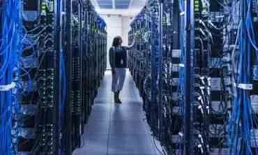 Person walking between rows of server racks in a data center.